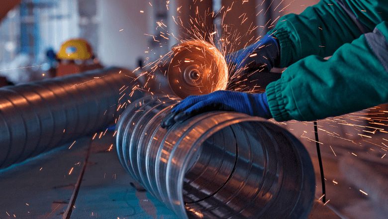 Operador industrial realizando corte de tubo de aço com disco abrasivo
